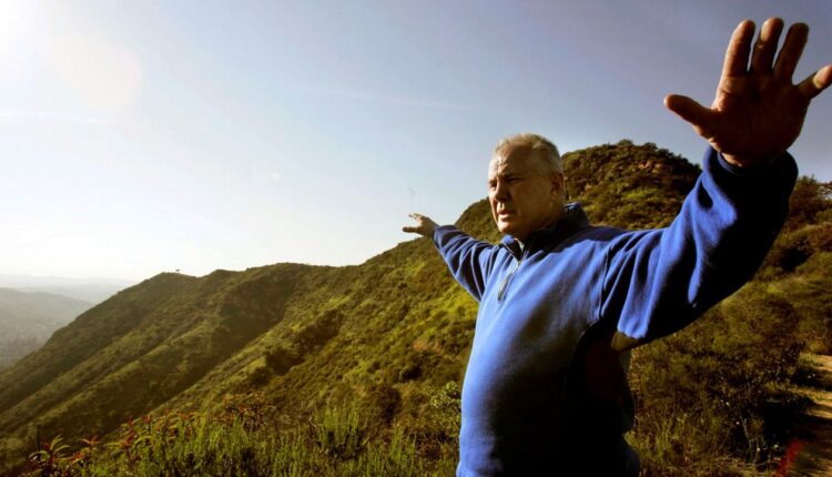 In this March 18, 2008, file photo, Los Angeles city councilman Tom LaBonge stands atop Mount Lee with Cahuenga Peak in the distance and near the famous Hollywood sign in Los Angeles. (AP Photo/Don Ryan)