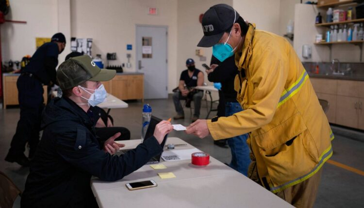 Firefighter Henry Hsieh, right, picks up a vaccination card before getting his second dose of the COVID-19 vaccine at a fire station in Los Angeles on Jan. 27, 2021. (AP Photo/Jae C. Hong)