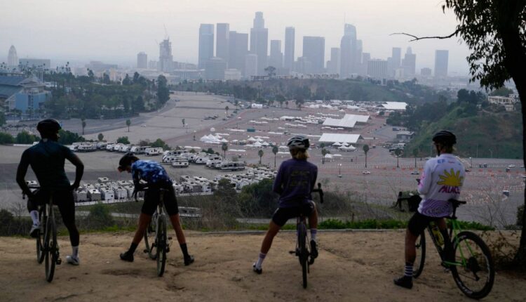 In this Feb. 11, 2021, file photo, cyclists rest atop a lookout point over a vaccination site at Dodger Stadium in Los Angeles. (AP Photo/Marcio Jose Sanchez)