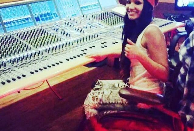 Woman+with+red+handkerchief+on+her+head+sits+at+soundboard+with+many+buttons.