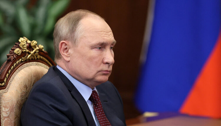 Vladimir Putin is seen sitting in a chair, looking across a table.