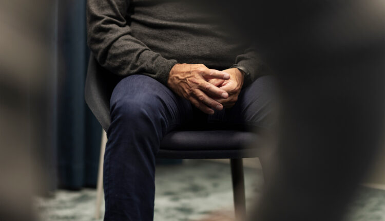 A shows a man's mid-section, sitting in a chair with his hands together.